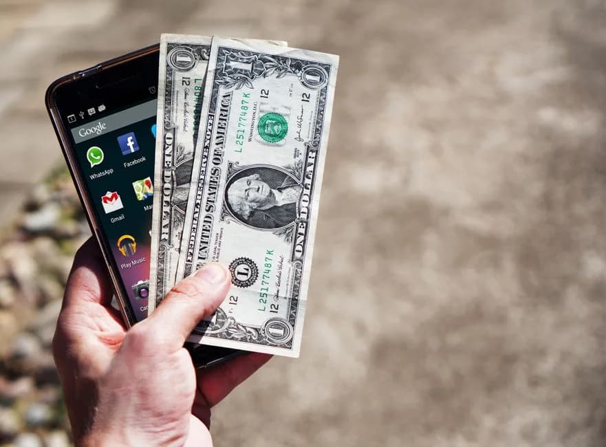 Hand holding a smartphone and US dollar bills representing mobile real money gaming
