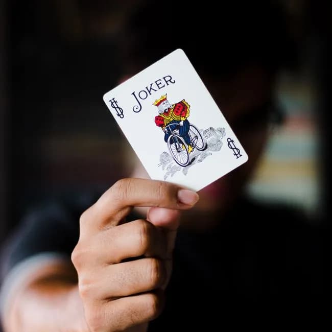 A person holding a Joker playing card, representing teen patti variant games