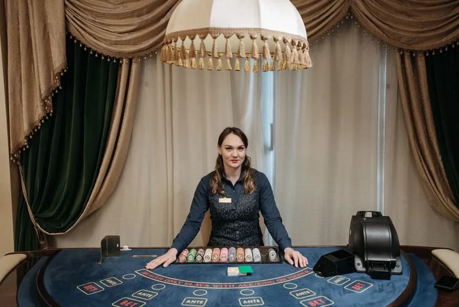 Smiling live dealer at a casino baccarat table surrounded by chips and cards