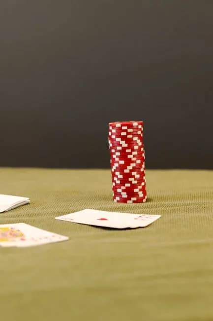 Red poker chips stacked with playing cards on a green felt table, representing cash rummy formats