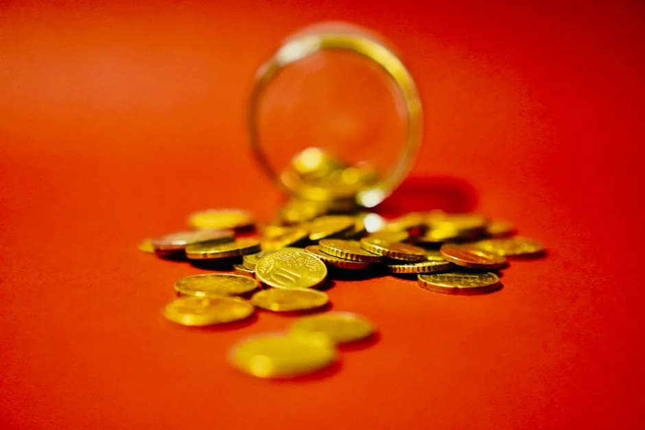 A collection of golden coins spilling from a glass jar on a red background