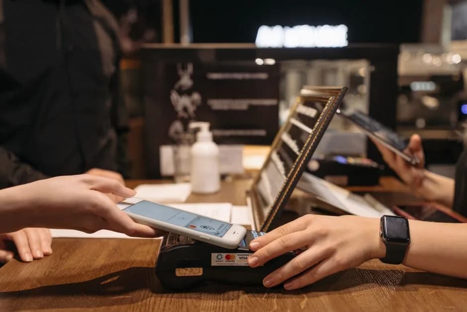 Person tapping mobile phone on a contactless payment terminal at a cafe