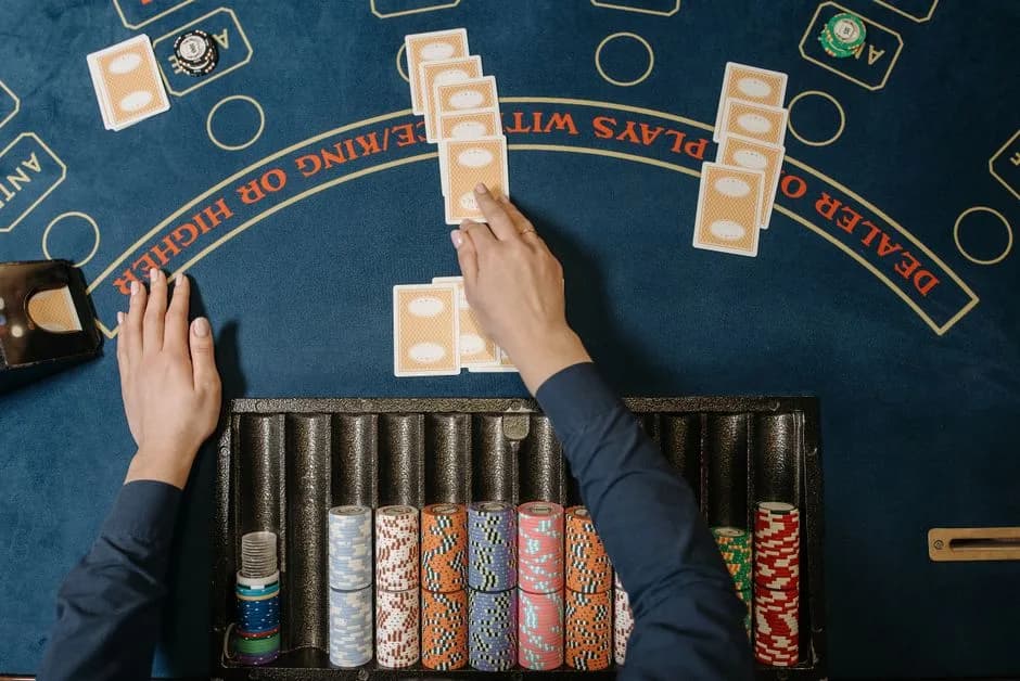 Casino dealer holding playing cards at a blackjack-style table with chips visible
