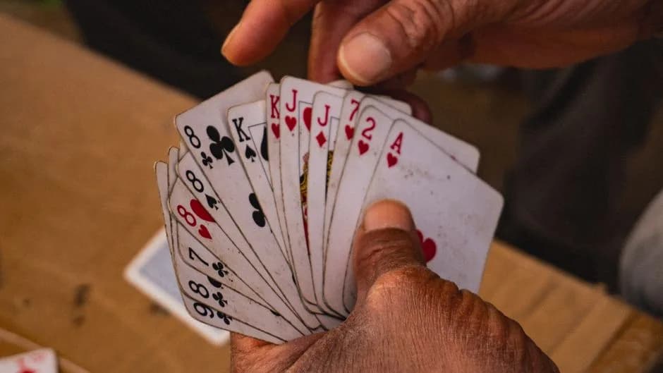 Hands holding playing cards in a rummy game